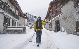 Skieuse qui marche dans une ruelle enneigée d'Argentière avec ses skis à la main